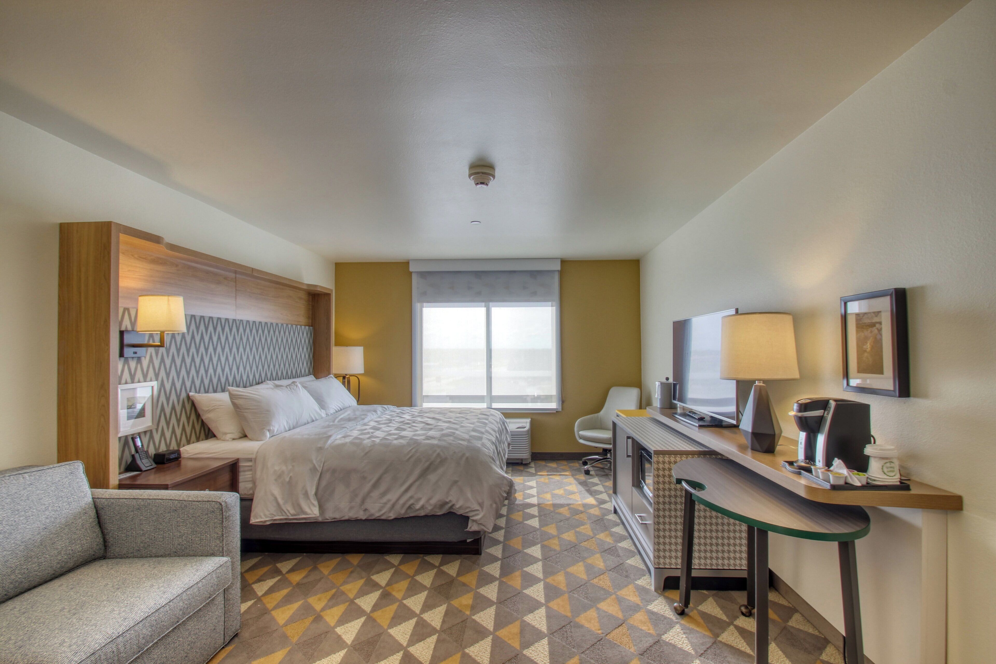 A hotel room with a bed, a desk, a chair, a TV, and a coffee machine.