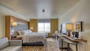 A hotel room with a bed, a desk, a chair, a TV, and a coffee machine.