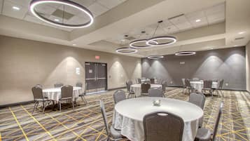 Un salón de conferencias con mesas y sillas redondas, una alfombra estampada y luces de techo circulares modernas.