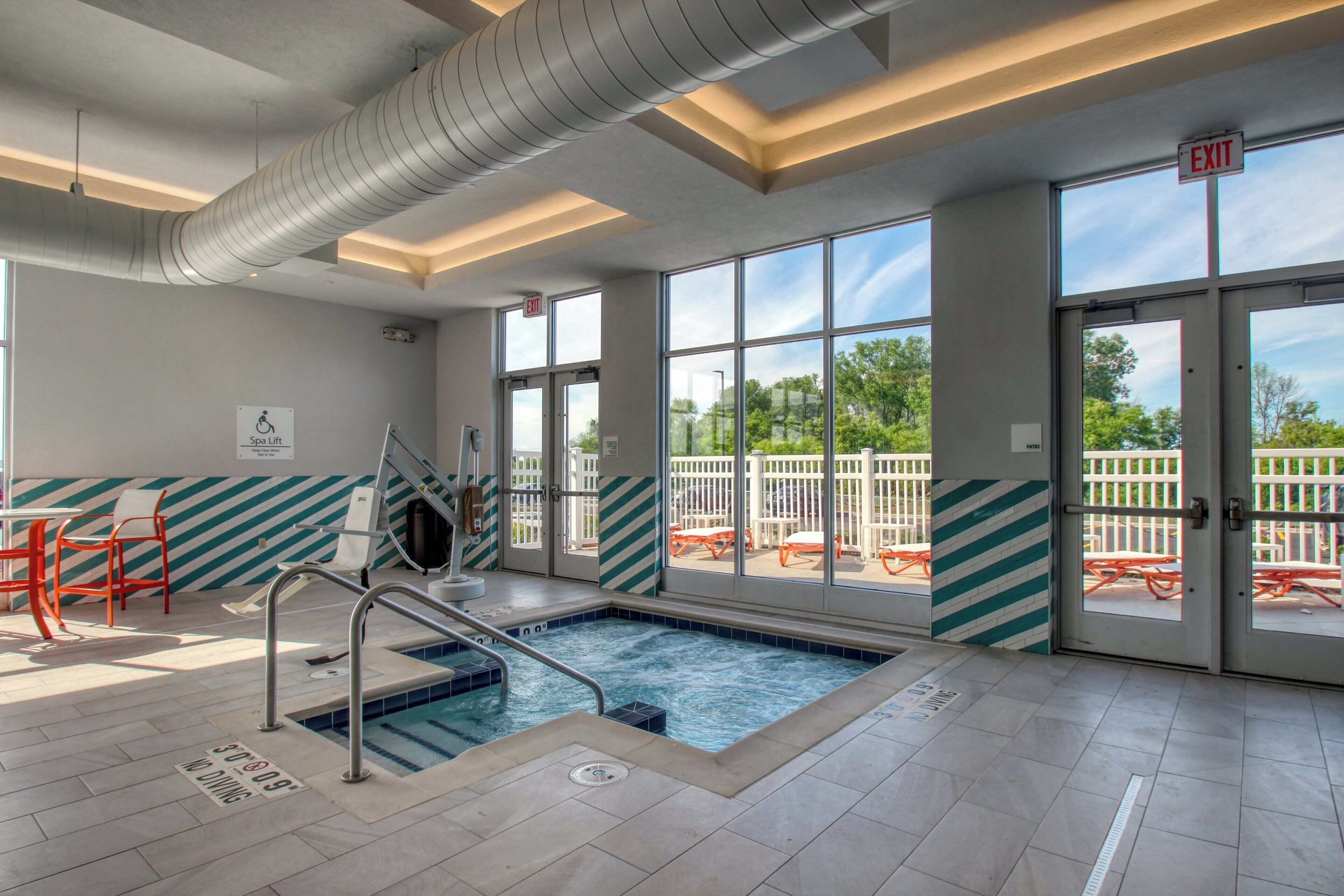 An indoor swimming pool with clear glass doors leading to an outdoor patio area.
