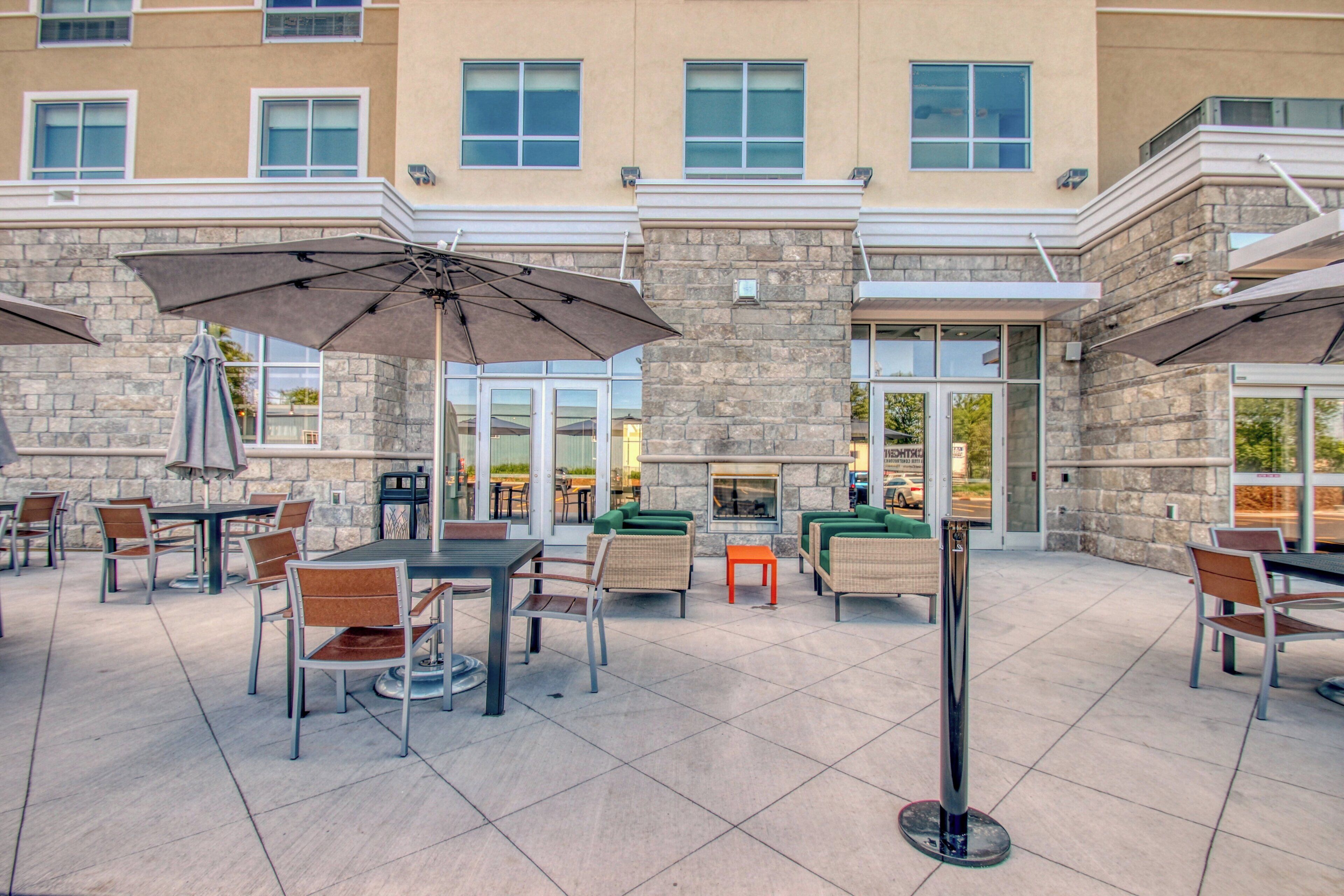 An outdoor patio area with tables and chairs, umbrellas, and a stone building facade.