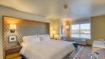 A hotel room with a large bed, two bedside tables, a chair, a desk, and a window with a view.