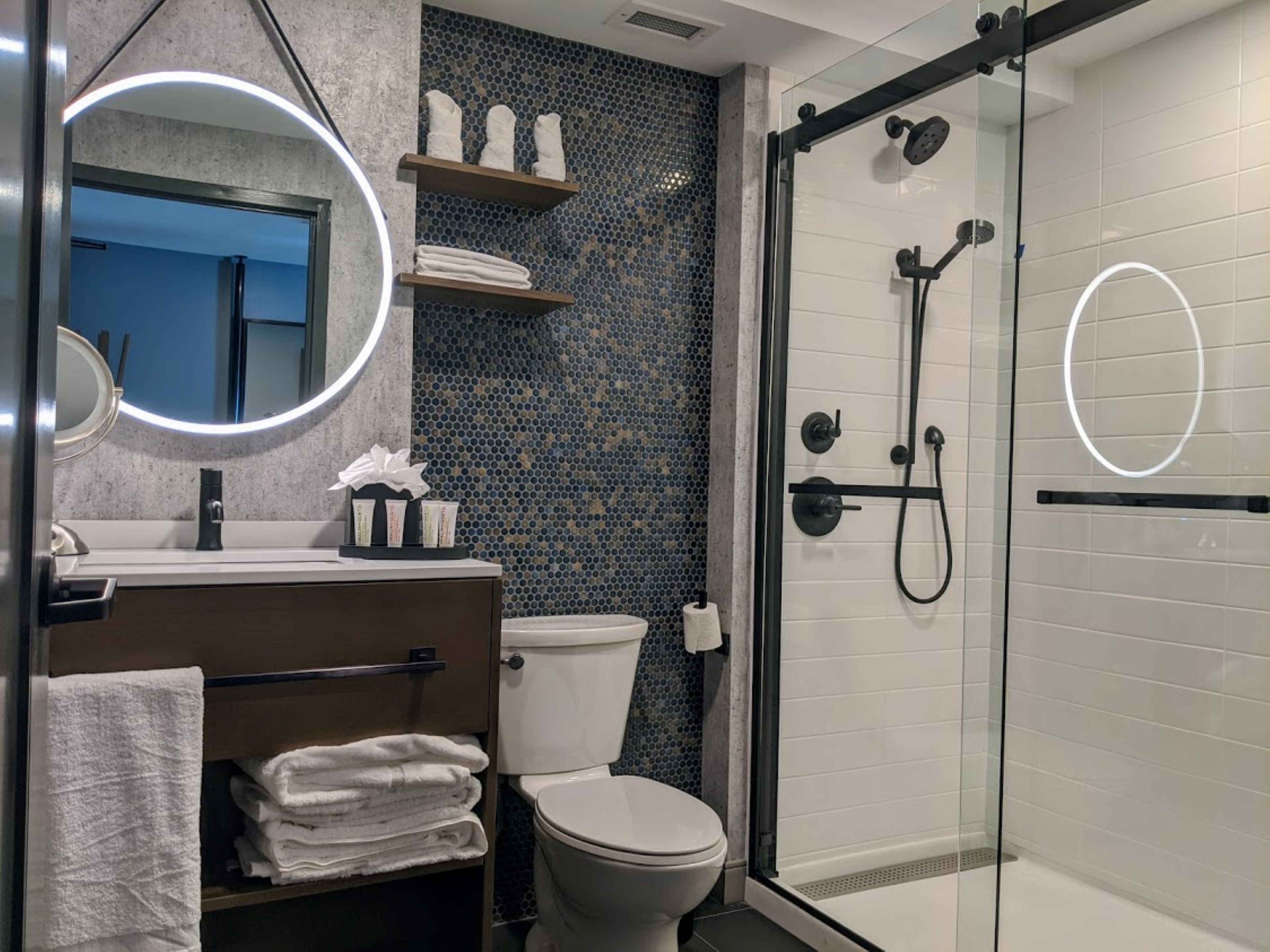 A modern bathroom with a glass-enclosed shower, a round mirror, and a toilet.