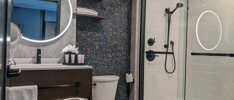 A modern bathroom with a glass-enclosed shower, a round mirror, and a toilet.