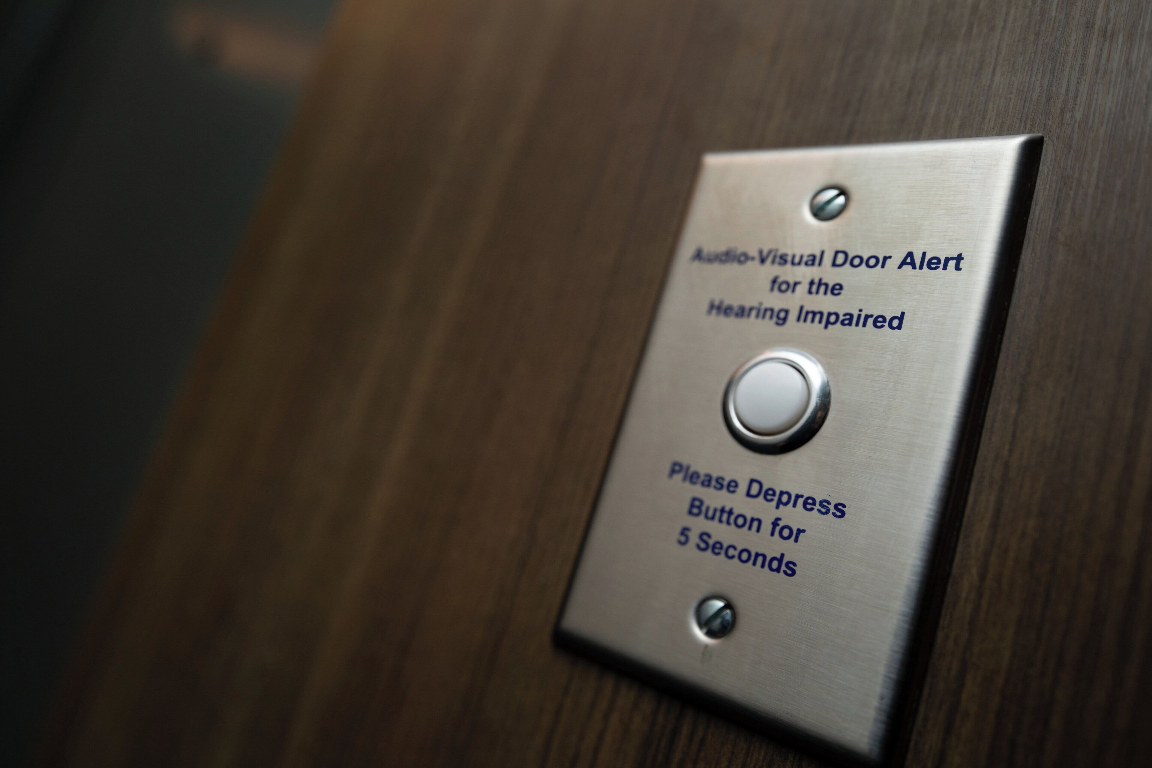 Placa metálica con alerta audiovisual para personas con discapacidad auditiva y un botón para accionar durante 5 segundos.