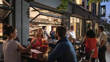 An outdoor seating area with tables and chairs, a glass enclosure for a food service counter, and a sign indicating the establishment is a hotel.