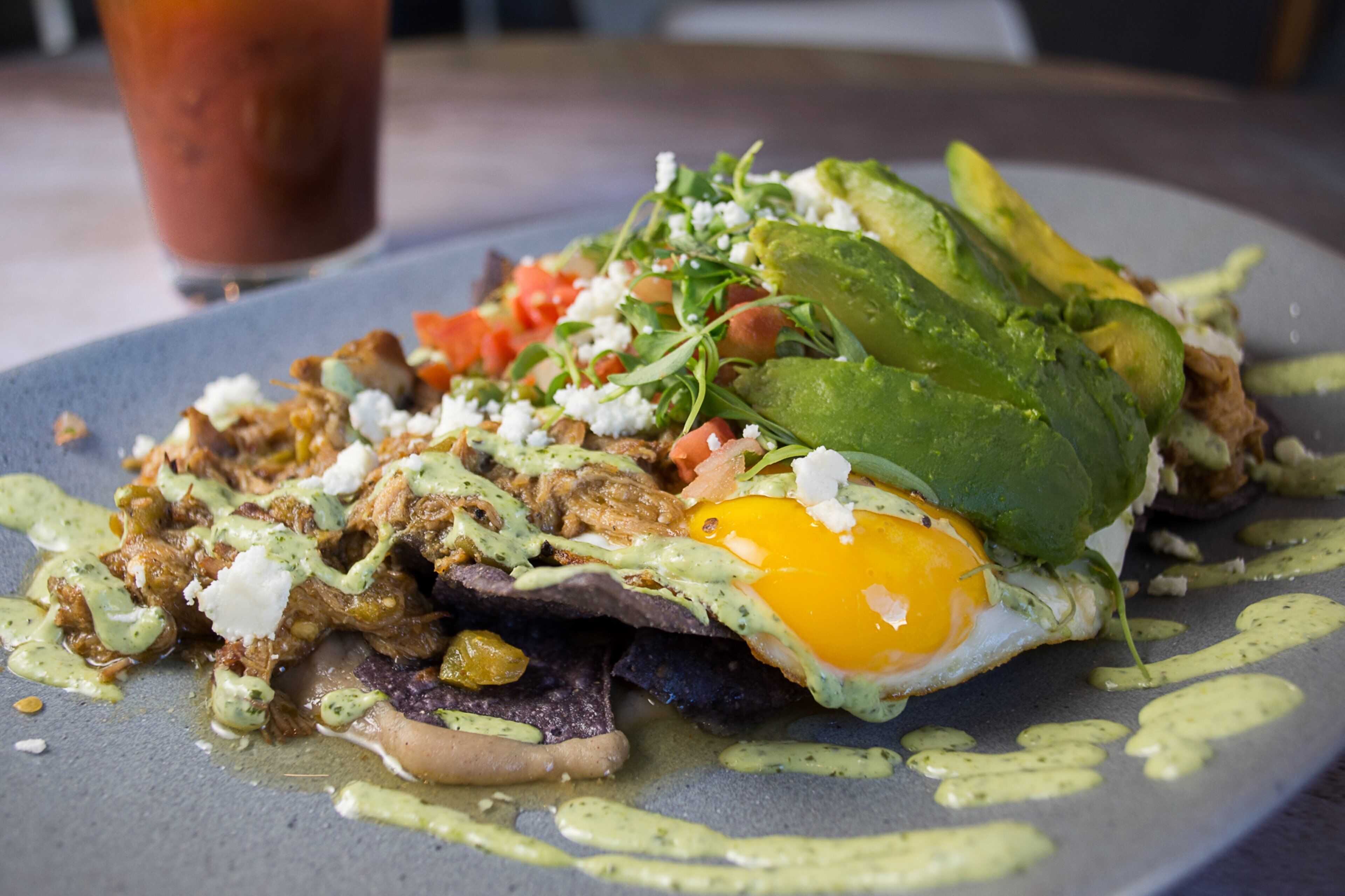 A plate of food with an egg, avocado, and greens.
