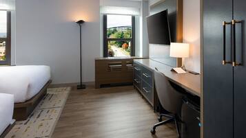 Ett hotellrum med en säng, ett skrivbord, en stol och en tv.