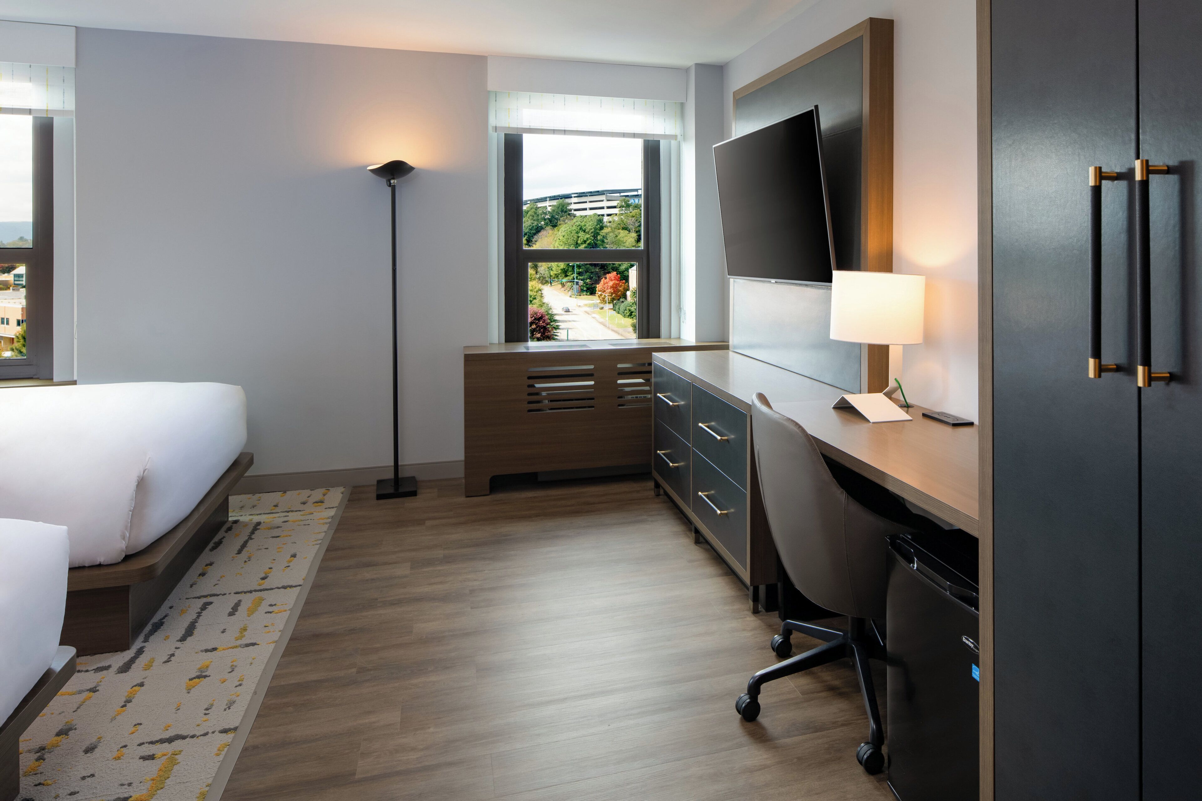 Een hotelkamer met een bed, bureau, stoel, kledingkast, televisie en een raam met uitzicht.