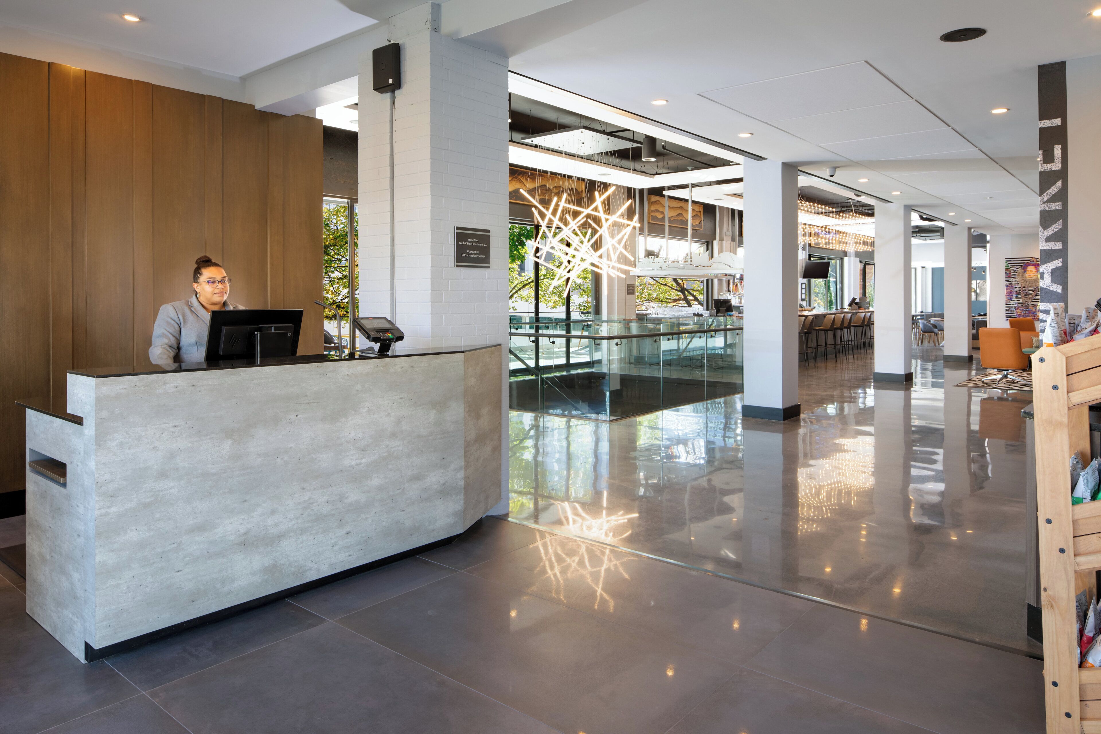 Balcão de atendimento moderno com recepcionista, divisória de vidro e vista para o interior.