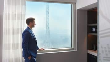 A man in a blue suit standing by a window with a view of a tall tower.