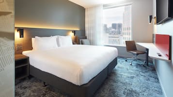 A hotel room with a large bed, a desk, a chair, and a TV.