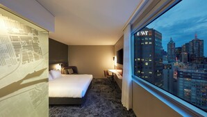 A hotel room with a bed, a desk, and a view of a cityscape. - Holiday Inn Express Melbourne Southbank by IHG (Southbank)