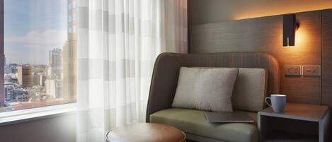 Habitación de hotel moderna con vistas a la ciudad, un sofá con almohadas, una mesita con una taza y una lámpara.