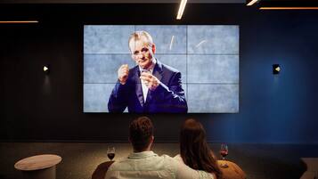 A cinema with a large screen displaying a movie, a person in the foreground, and a woman with a wine glass.