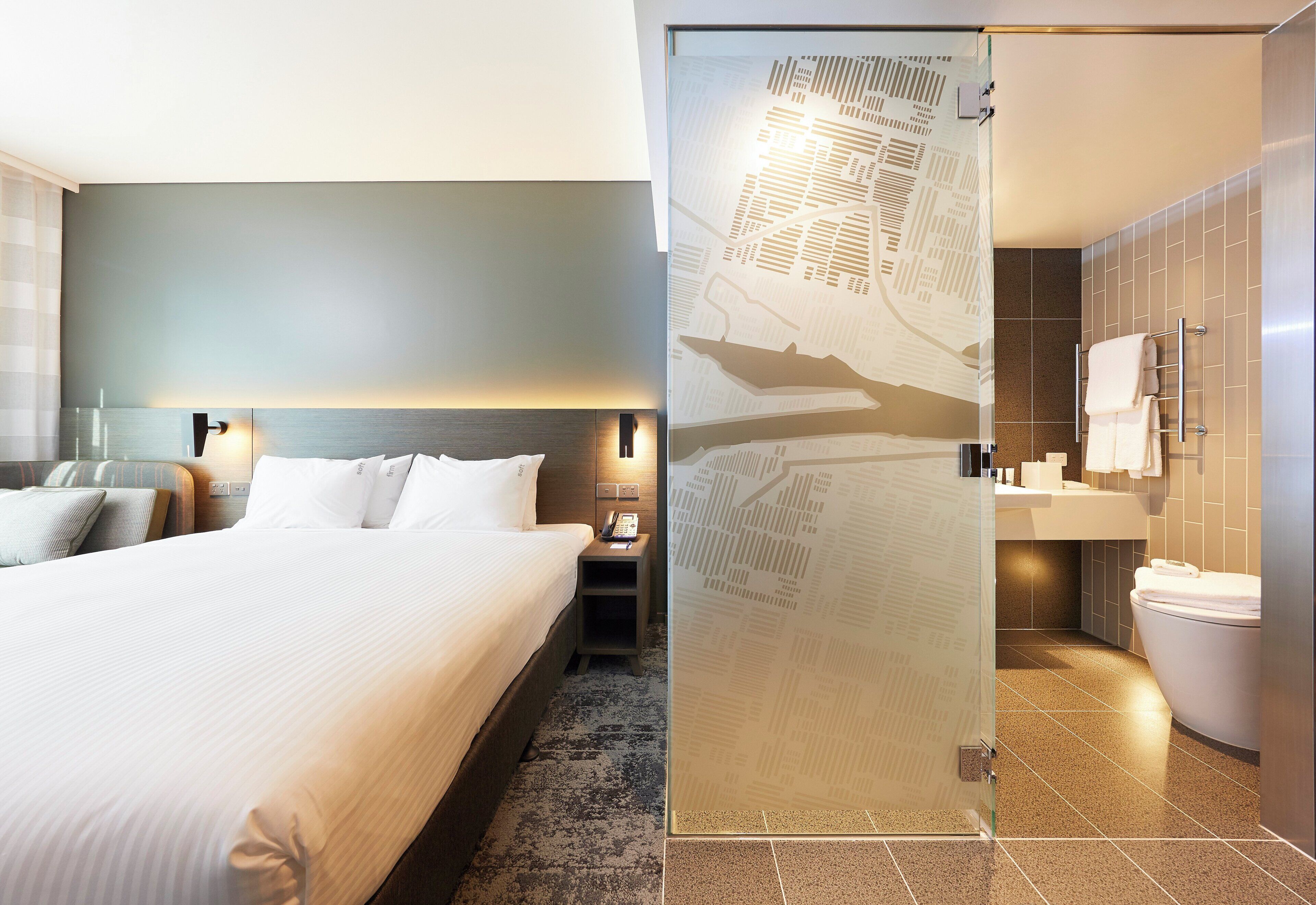 Una habitación de hotel con cama, mesita de noche y baño con inodoro y lavabo.