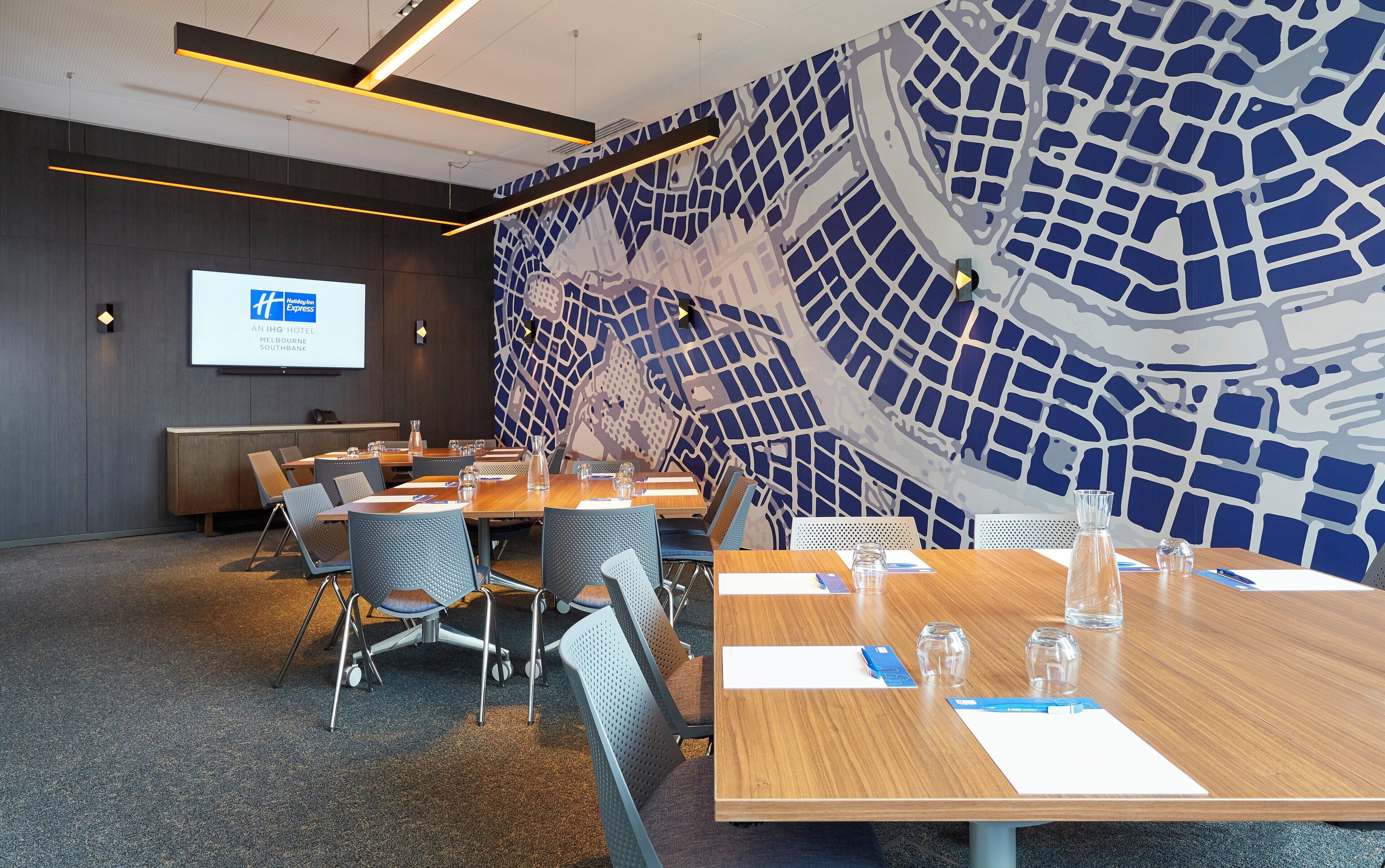 Sala de conferência com mesas, cadeiras e tela para apresentação.