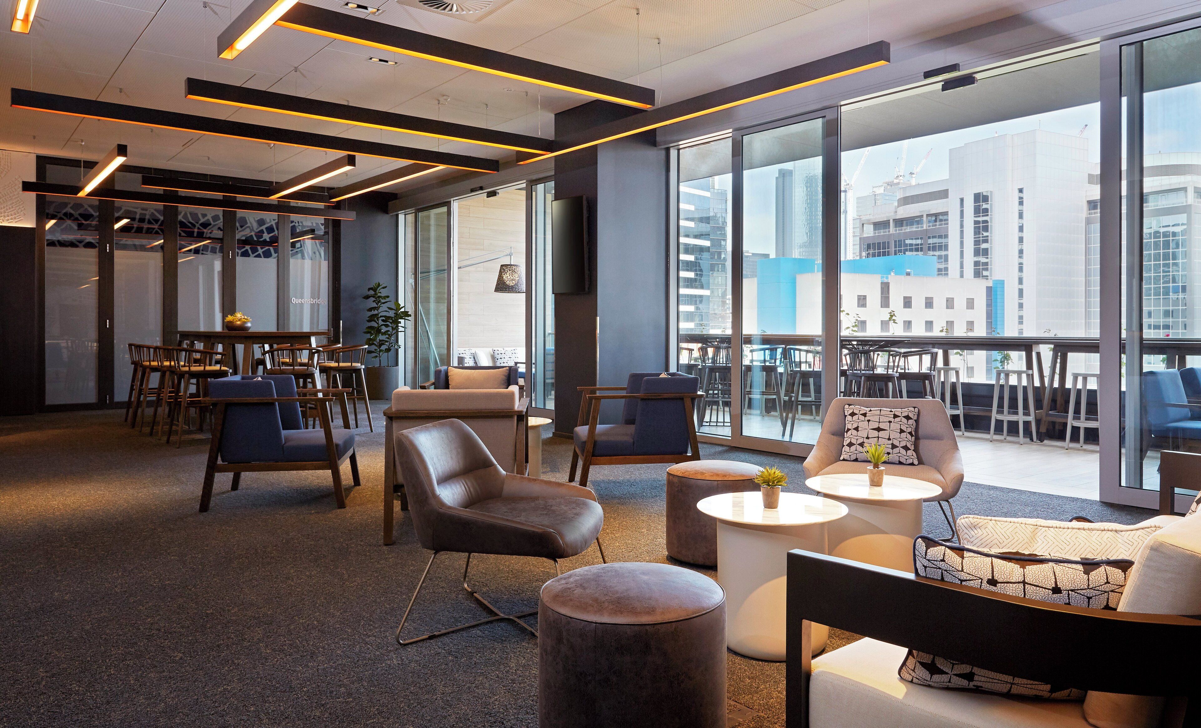 A modern office space with a mix of seating arrangements, including chairs and sofas, and a large window providing a view of the cityscape.