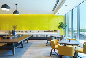 A modern dining area with a long counter, multiple seating options, and a view through large windows. - Holiday Inn Express Melbourne Southbank by IHG (Southbank)