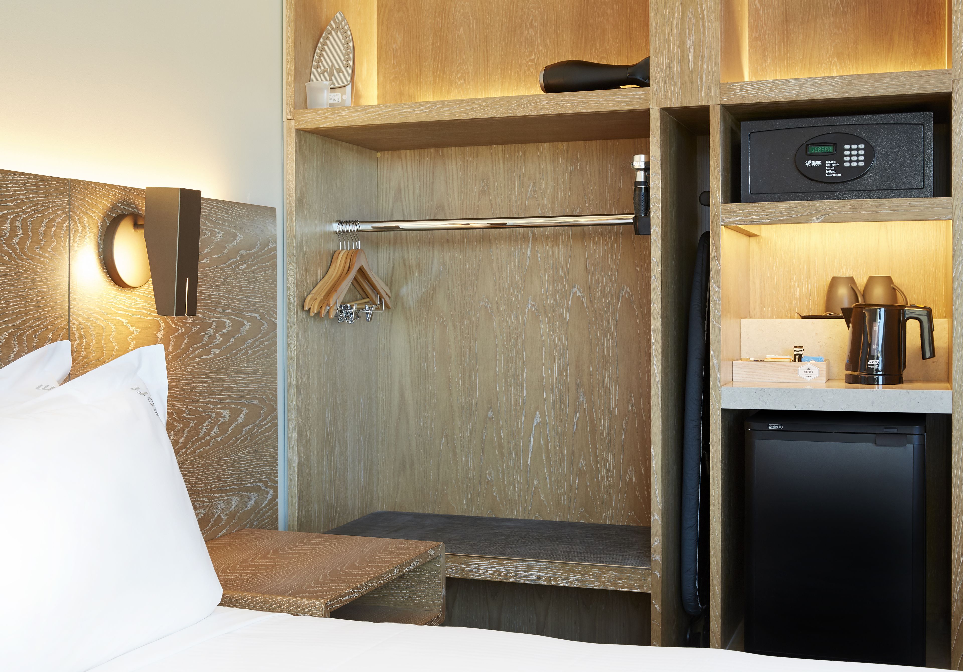 Quarto de hotel compacto com cama, um pequeno espaço para sentar, cafeteira embutida e mini-geladeira.