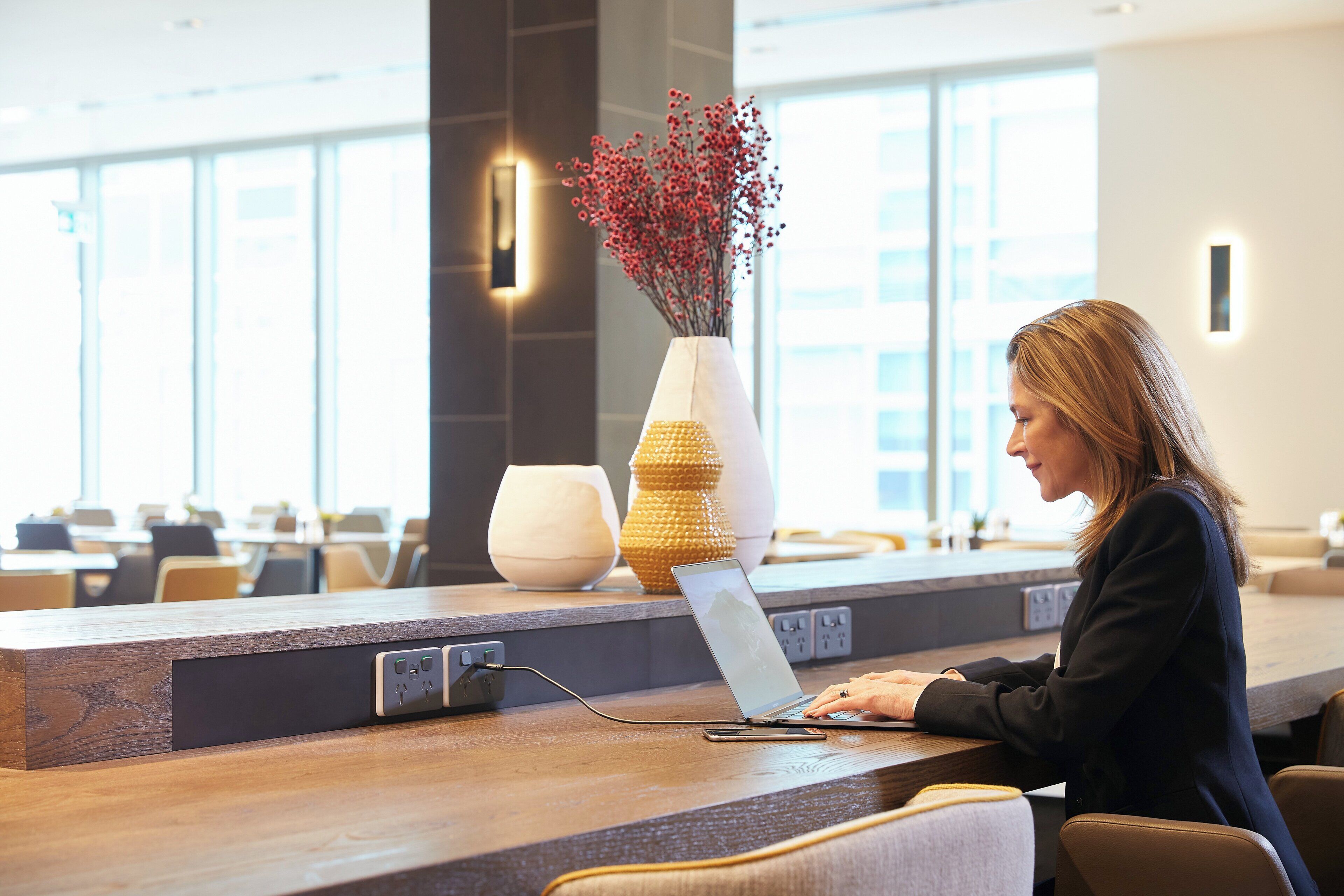 A person working on a laptop at a reception desk with a vase of red flowers and a textured lamp.