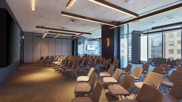 A conference room with rows of chairs, a large window with a cityscape view, and modern ceiling lighting.