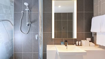 Uma casa de banho moderna com chuveiro, lavatório e espelho.