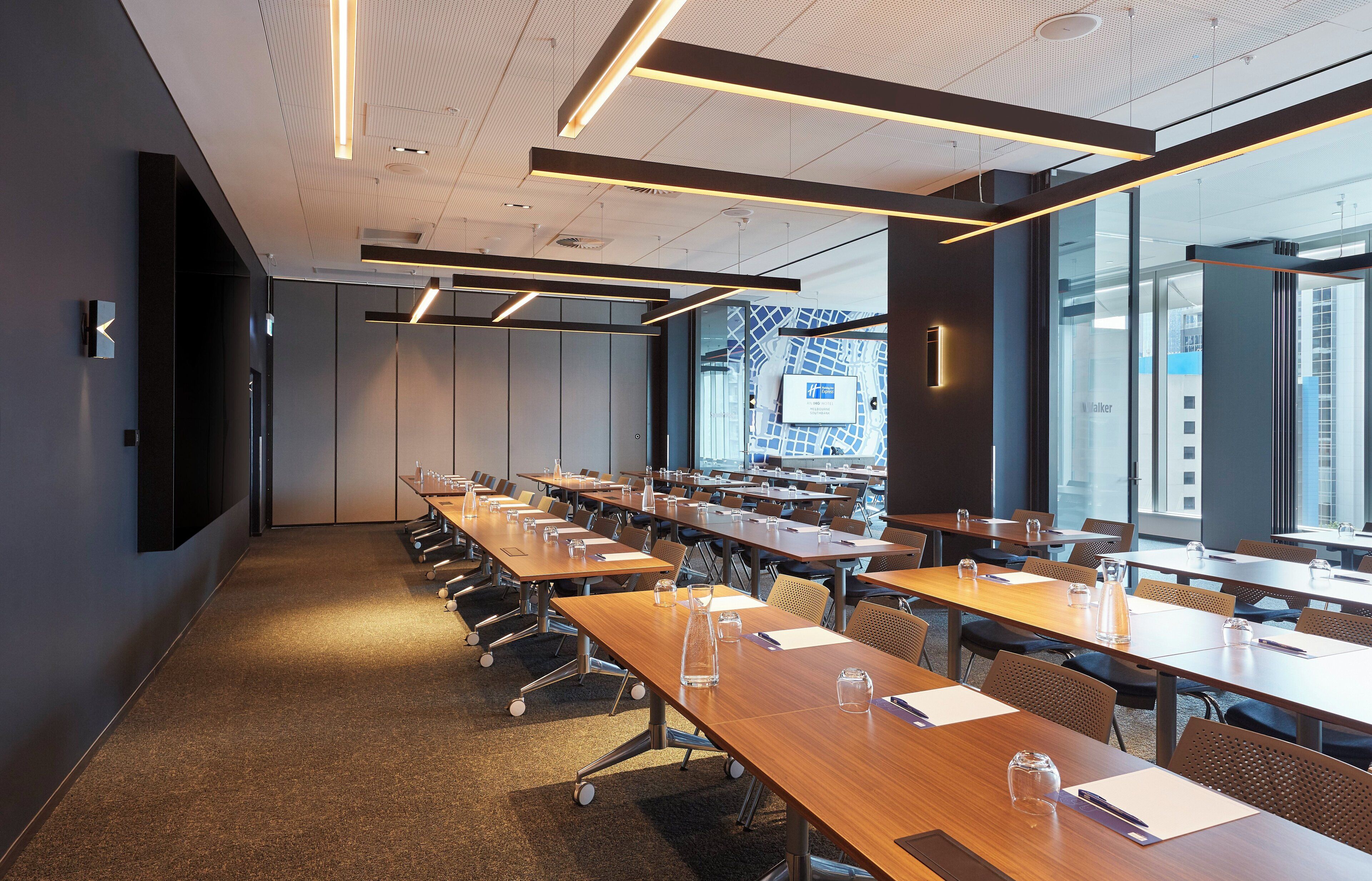 A conference room with multiple tables and chairs, large windows, and a modern ceiling design.