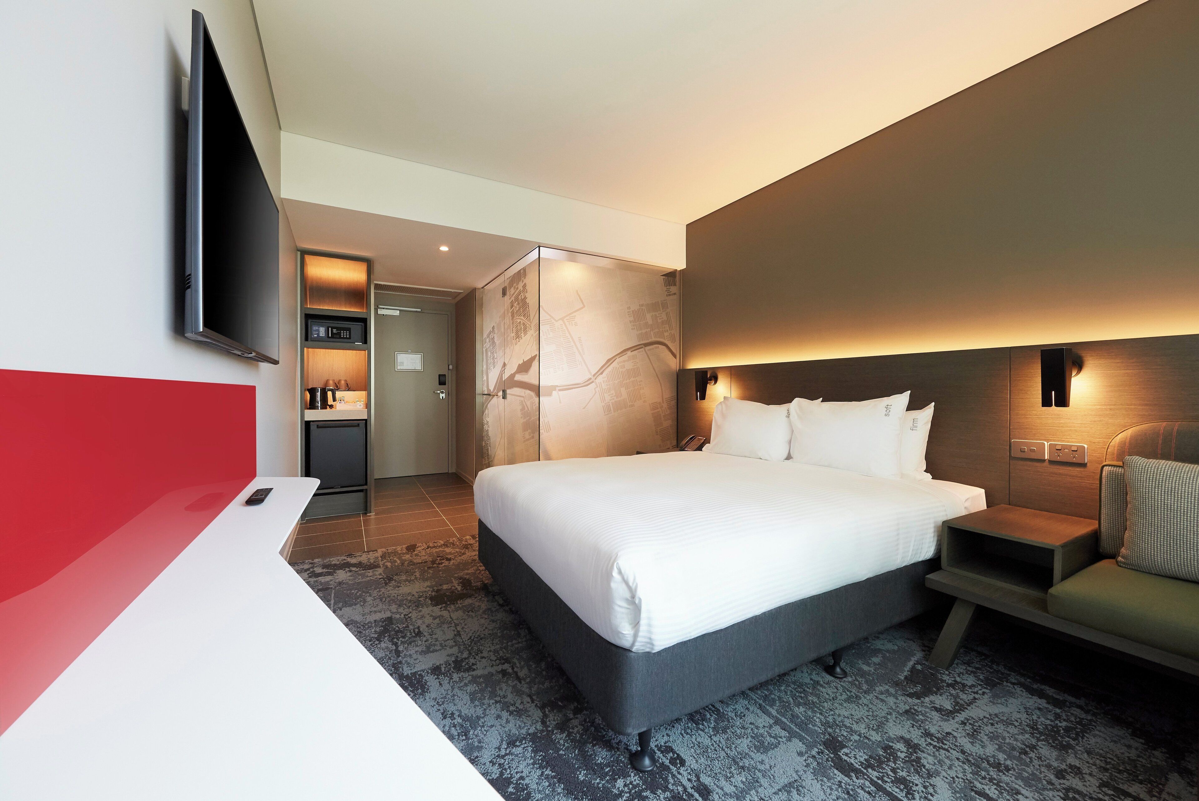 A modern hotel room with a large bed, a flat-screen TV, a small desk, and a seating area.