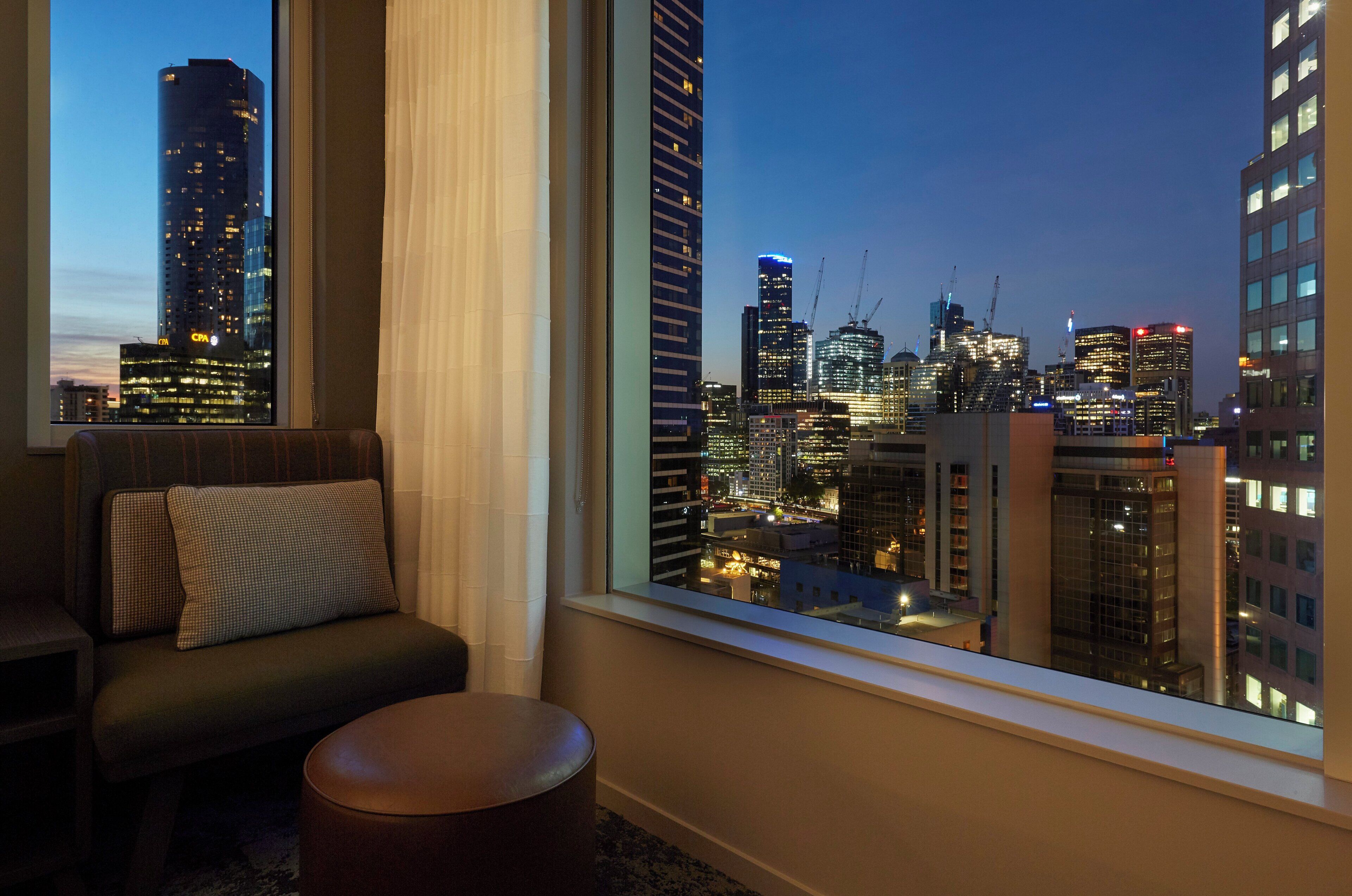 A room with a view of a city skyline at dusk, featuring modern buildings and construction cranes.