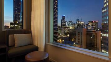 A room with a view of a city skyline at dusk, featuring modern buildings and construction cranes.