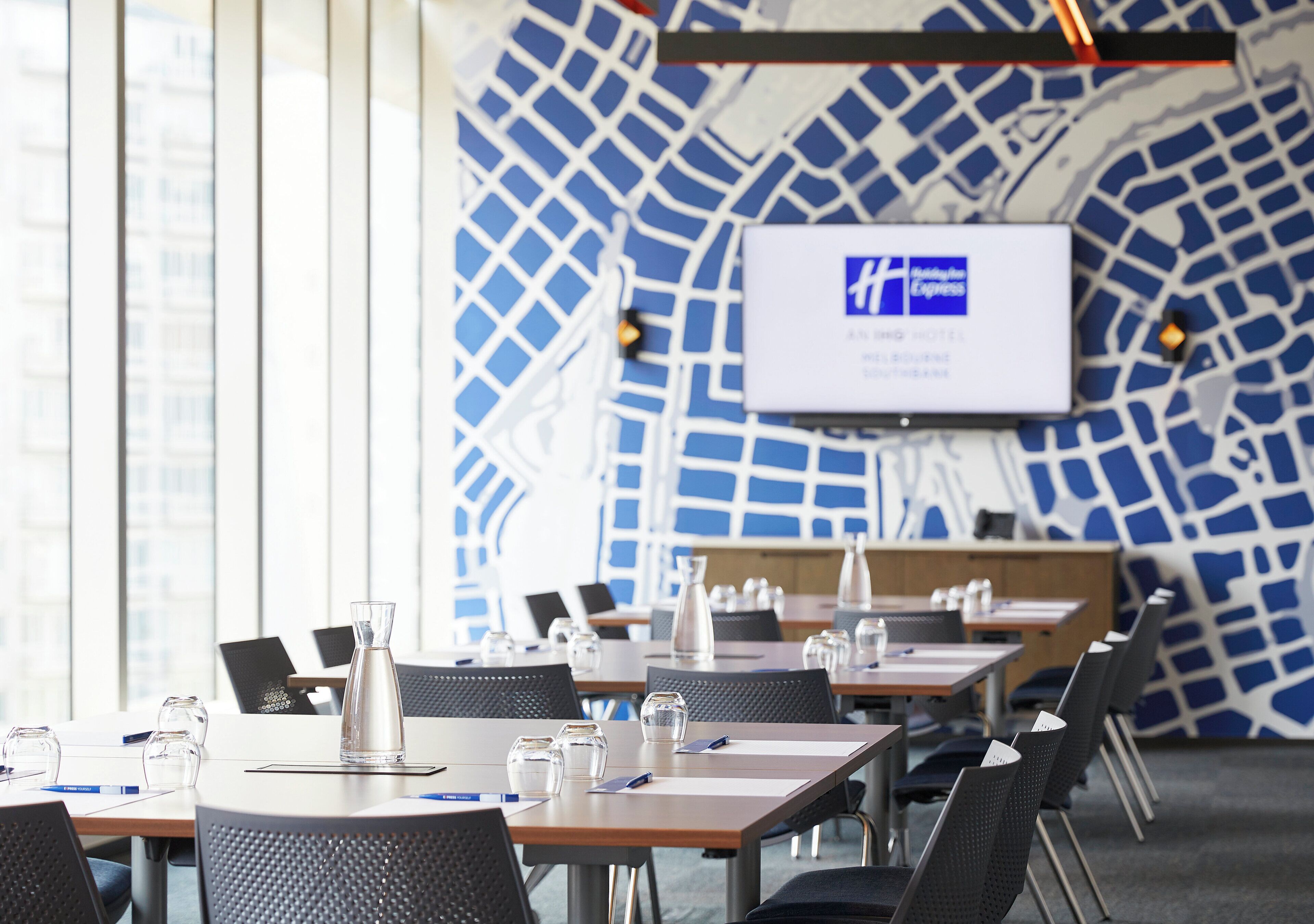 A conference room with tables, chairs, and a projection screen displaying a logo.