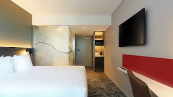 Quarto de hotel com uma cama grande, televisão na parede, parede de destaque vermelha e uma pequena área de escritório.
