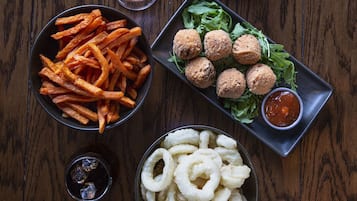 A wooden table with bowls of fries, fried balls, onion rings, and a small bowl of sauce.