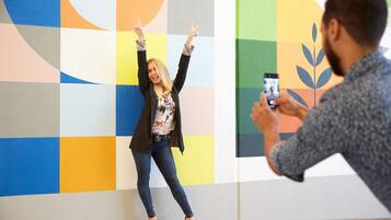 Una persona fotografiando a otra frente a una pared con diseños geométricos y colores vibrantes.