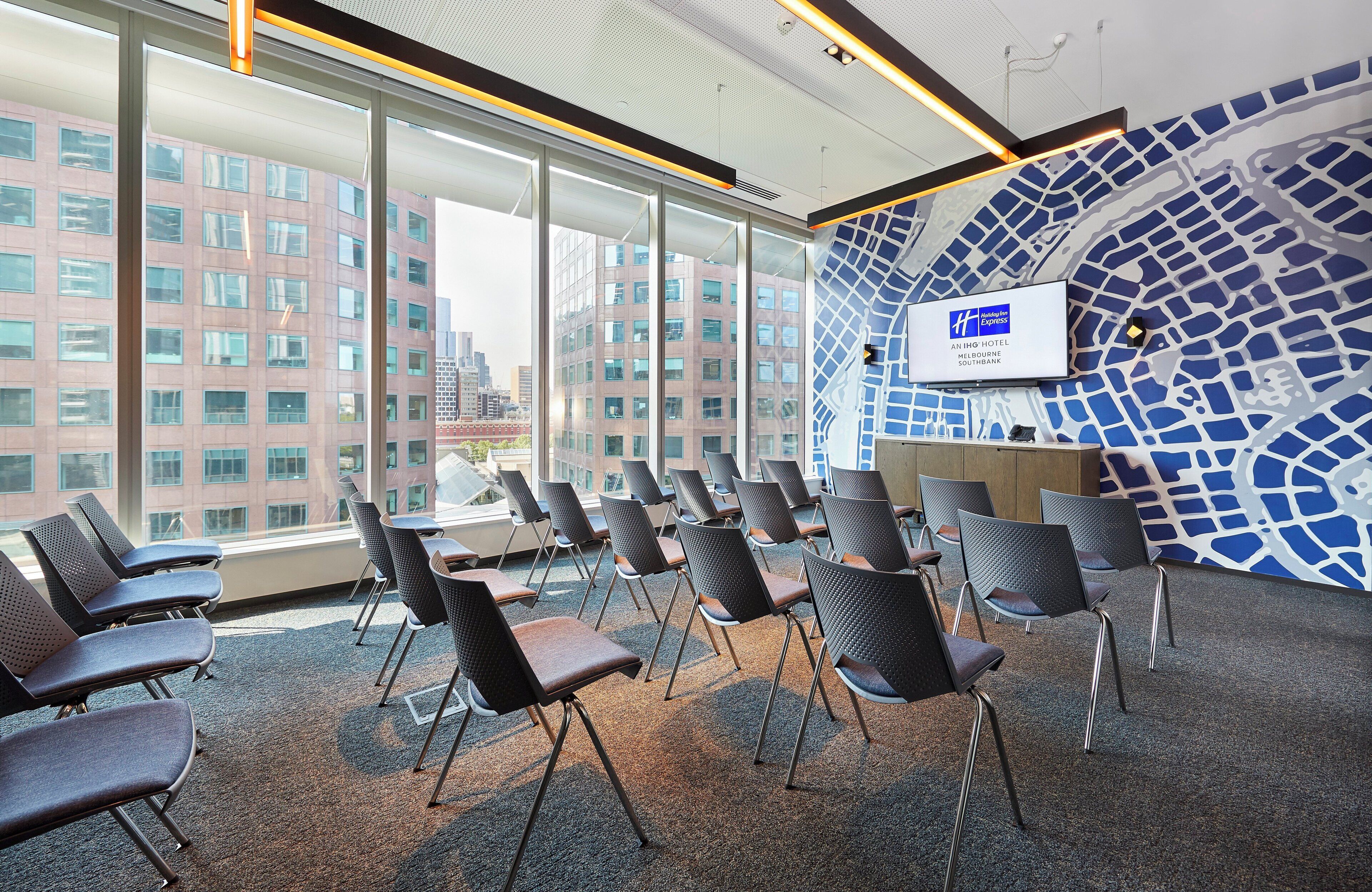 A hotel lobby with a large TV screen, seating area, and a view of the cityscape.