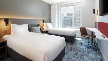 A hotel room with two beds, a desk, a chair, and a large window with a city view.