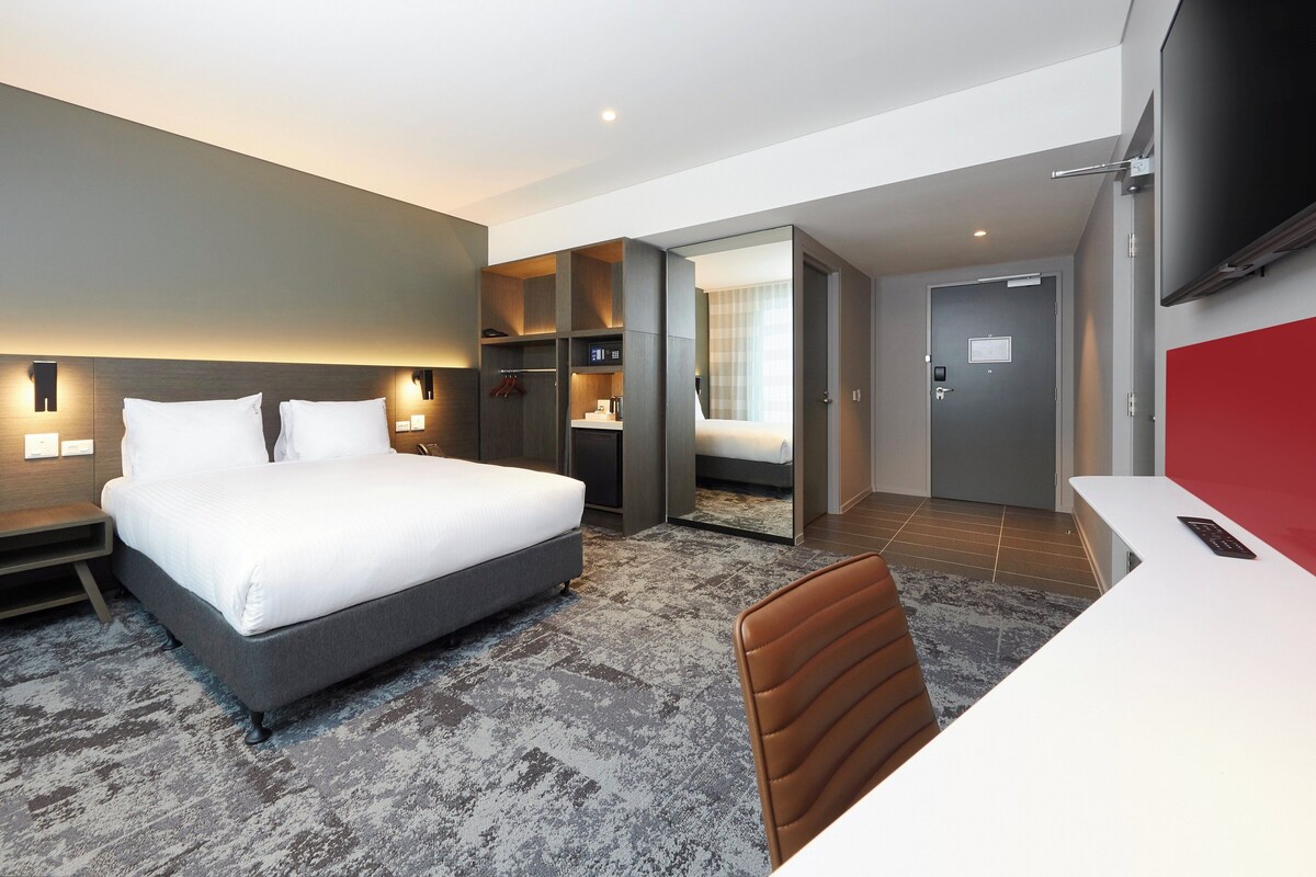 A modern hotel room with a large bed, bedside tables, a desk, and a TV.
