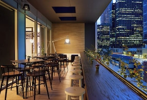 A modern interior with wooden flooring, tables, and chairs, a large window with a view of a cityscape at night. - Holiday Inn Express Melbourne Southbank by IHG (Southbank)