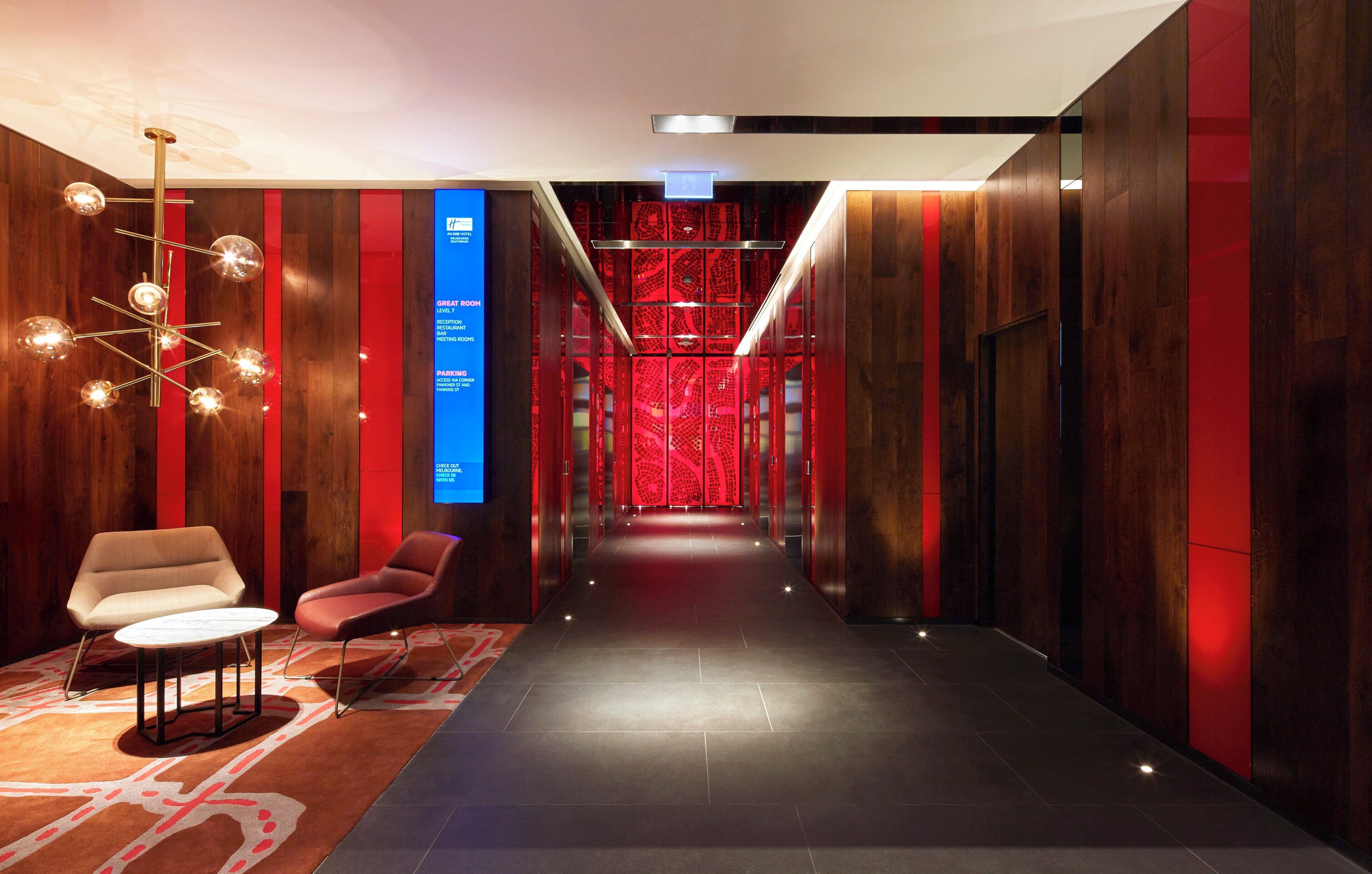 A hotel corridor with a reception desk, seating area, and a digital directory.