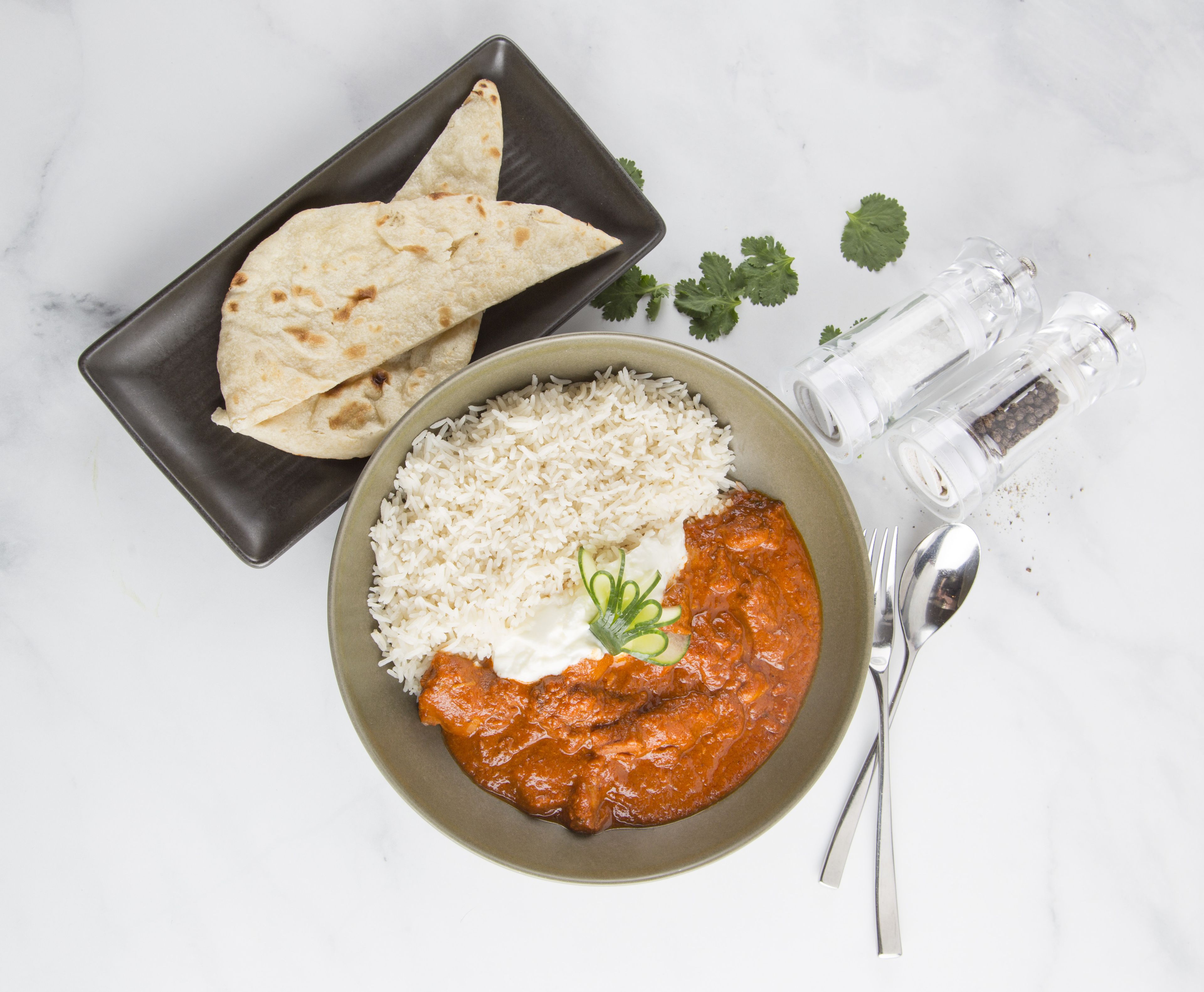 A bowl of curry with rice and naan bread on a plate, accompanied by a salt shaker and a spoon.
