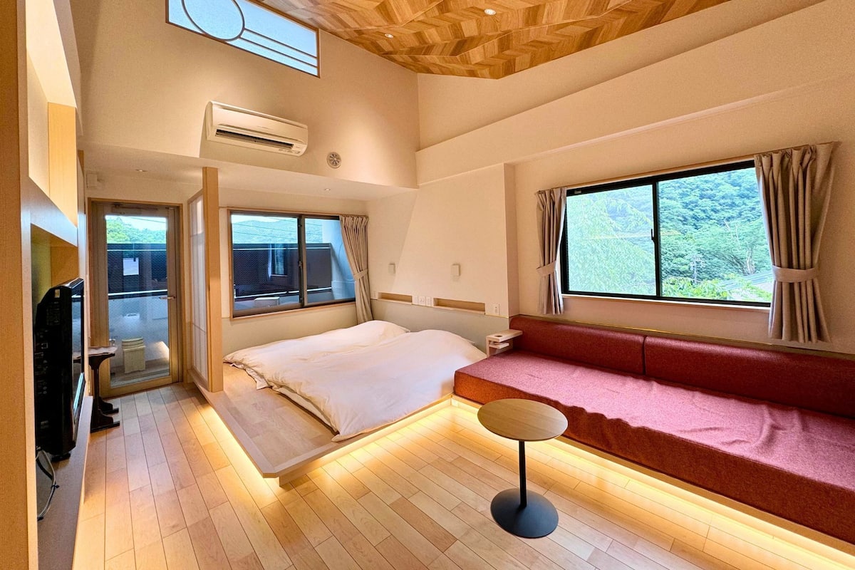 Une chambre d’hôtel moderne, équipée d’un lit, d’une petite table ronde, d’un canapé, d’une télévision et d’une grande fenêtre avec des rideaux.
