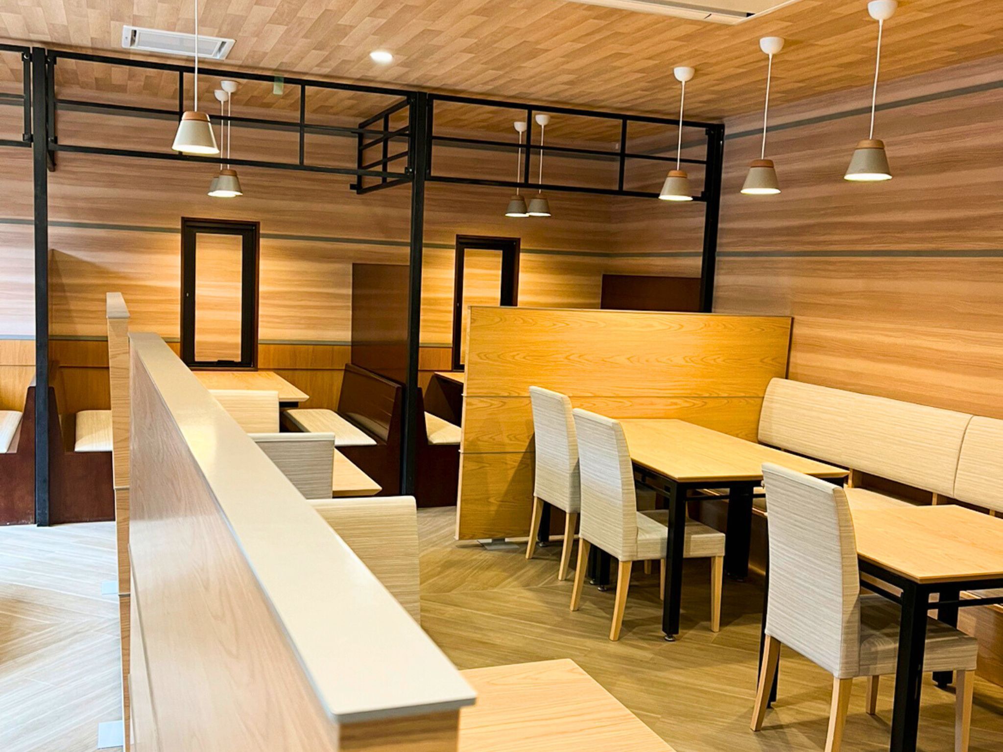 Un interior de restaurante moderno con paneles de madera, vigas de metal negro e iluminación colgante.