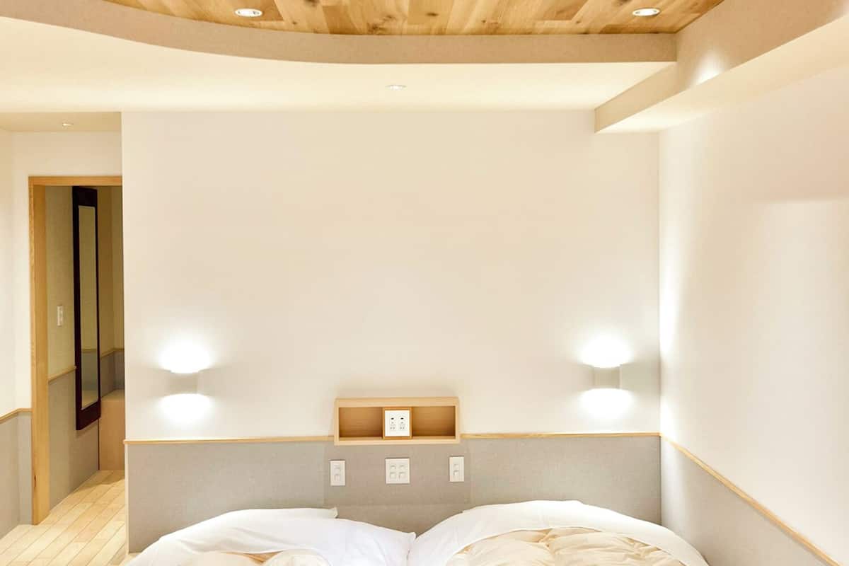 Une chambre moderne avec un plafond en bois, un lit recouvert de linge de lit blanc et un éclairage encastré.