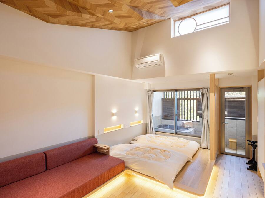 A modern hotel room with a wooden ceiling, a large bed, a red sofa, and a TV.
