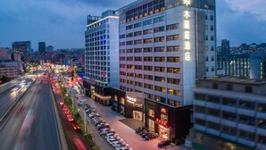 Um hotel moderno com uma placa de destaque, vários andares e um estacionamento com carros.