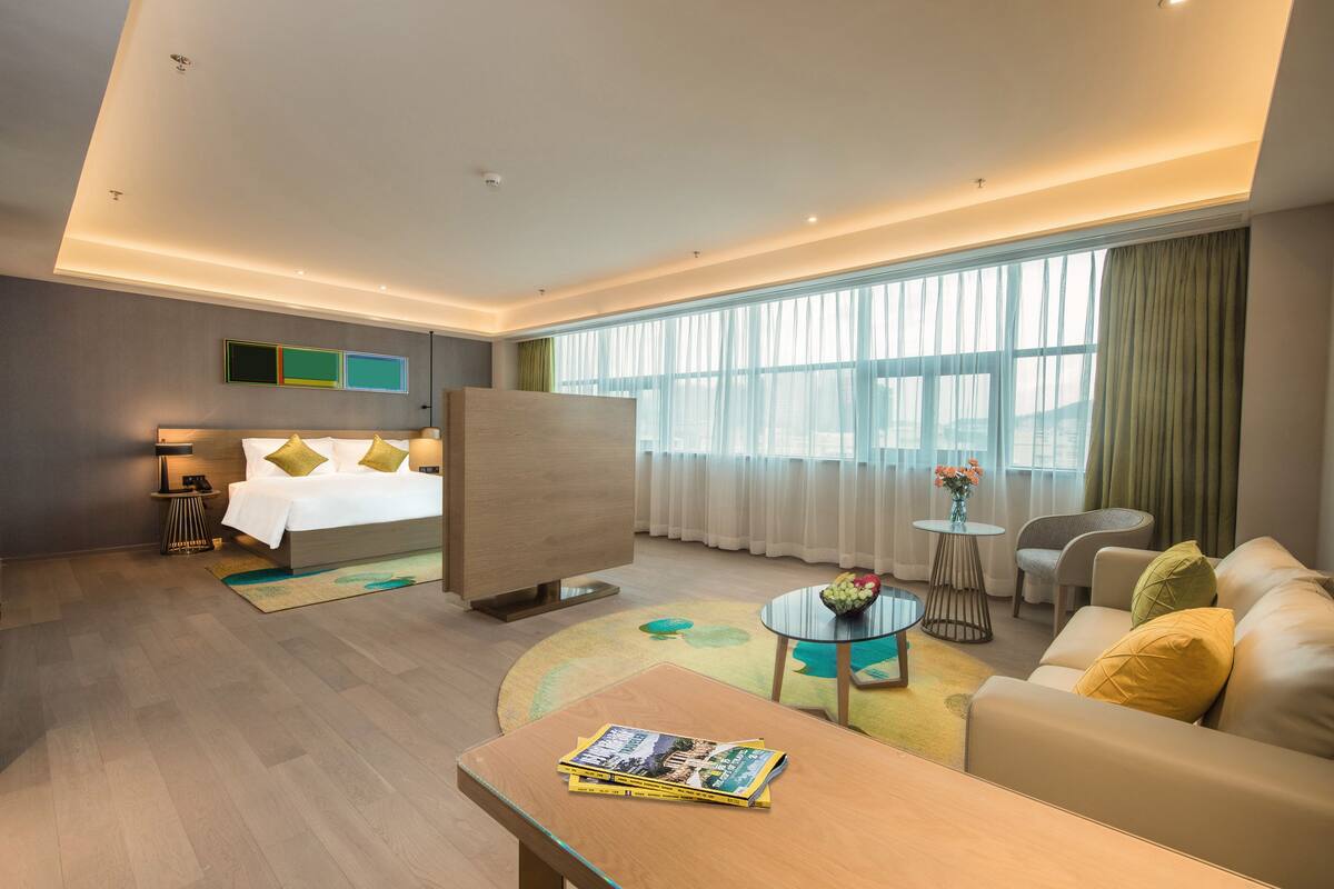A modern hotel room with a bed, a sofa, a coffee table, and a small table with a vase of flowers.