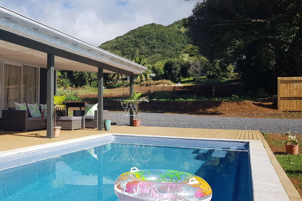 A pool area with a covered patio, outdoor furniture, and a view of a hilly landscape.