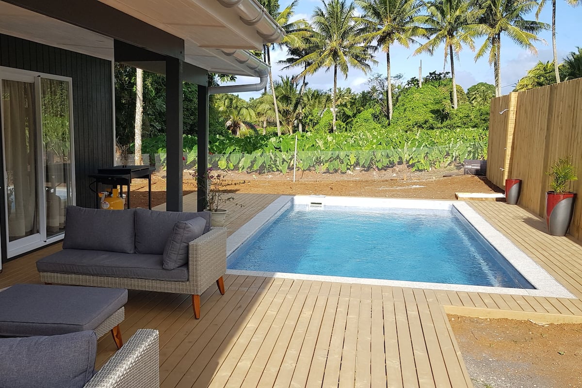 A covered outdoor area with a pool, seating, and a view of tropical vegetation.
