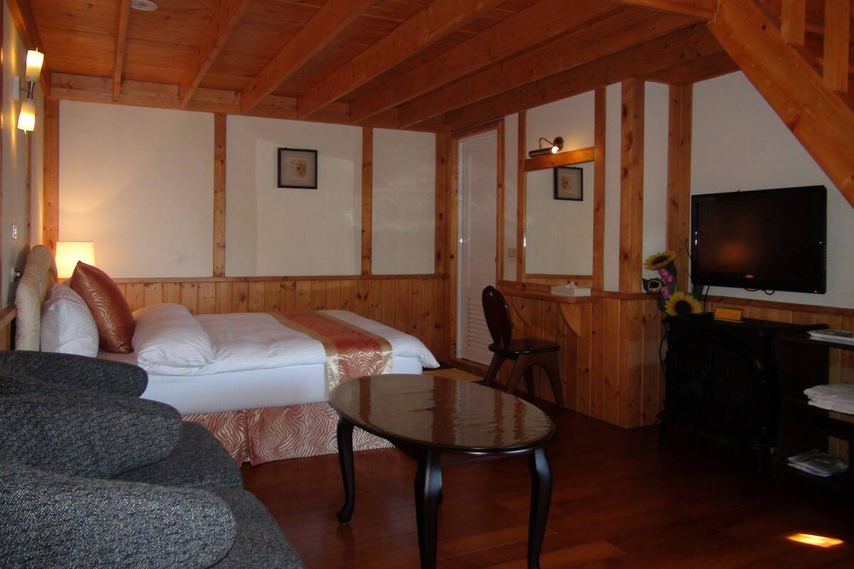 A cozy room with a bed, a sofa, a small table, a TV, and wooden walls.